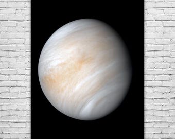 May include: A poster featuring a detailed image of the planet Venus against a black background. The planet is depicted with swirling cloud patterns in shades of white, cream, and light orange. The poster is displayed on a white brick wall.