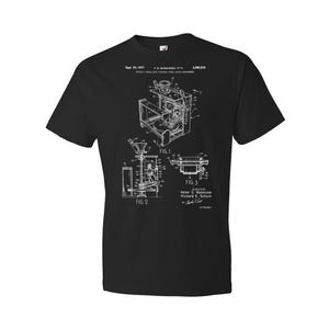 May include: Black t-shirt with a white graphic of a patent drawing for a coffee grinder. The drawing includes three figures and the text "Sept. 20, 1971", "1,605,218", "FIG. 1", "FIG. 2", "FIG. 3", "Peter D. Rasmusse", "Richard E. Schulz", and "ATTORNEY".