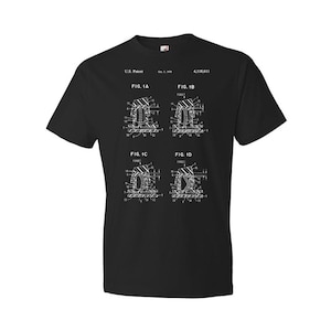 May include: Black t-shirt with a white print of a patent design for a mechanical device. The patent number is 4,118,611 and the patent date is Oct. 1, 1979. The design includes four diagrams labeled FIG. 1A, FIG. 1B, FIG. 1C, and FIG. 1D.