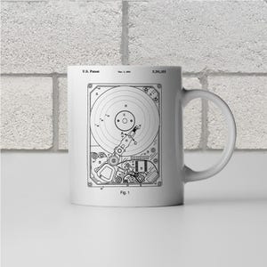 May include: A white ceramic mug with a black and white illustration of a hard drive patent. The patent number is 5,391,355 and the date is Mar. 1, 1995. The text "U.S. Patent" and "Fig. 1" are also included in the illustration.