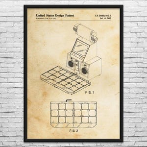 May include: A framed vintage patent print of an arcade game machine. The print features detailed technical drawings, including a top-down view of the game's control panel and a side view of the machine. The text "United States Design Patent" is visible.