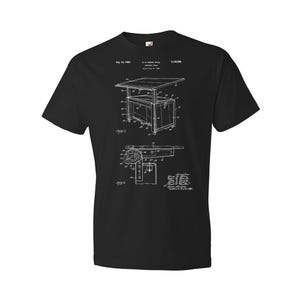 May include: Black t-shirt with a white print of a patent drawing for a drafting table. The patent number is 3,140,558 and the date is July 14, 1964.