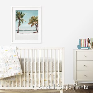 Op de afbeelding: Een wit babybedje met een grijs-wit gestreept lakentje en een wit-gele gestreepte rok. Een ingelijst printje van twee palmbomen op een strand hangt aan de muur achter het babybedje. Een witte commode met drie lades staat rechts in de afbeelding. Een blauwe speelgoedtruck met boeken erop staat op de commode. De tekst "Coastal Style Prints" staat onderaan de afbeelding.