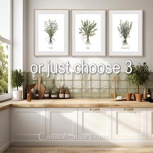 May include: Three framed botanical prints featuring watercolor illustrations of thyme, sage, and rosemary. Each print displays the herb's name below the image. The prints are displayed above a white cabinet and wooden countertop.