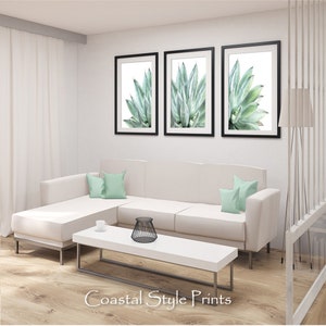 Pu&ograve; includere: Tre stampe incorniciate di una pianta di agave verde su sfondo bianco. Le stampe sono appese a una parete bianca sopra un divano angolare bianco con cuscini di colore verde chiaro. Il divano si trova in un soggiorno con un tavolino da caff&egrave; bianco e un oggetto decorativo in metallo nero sul tavolo.