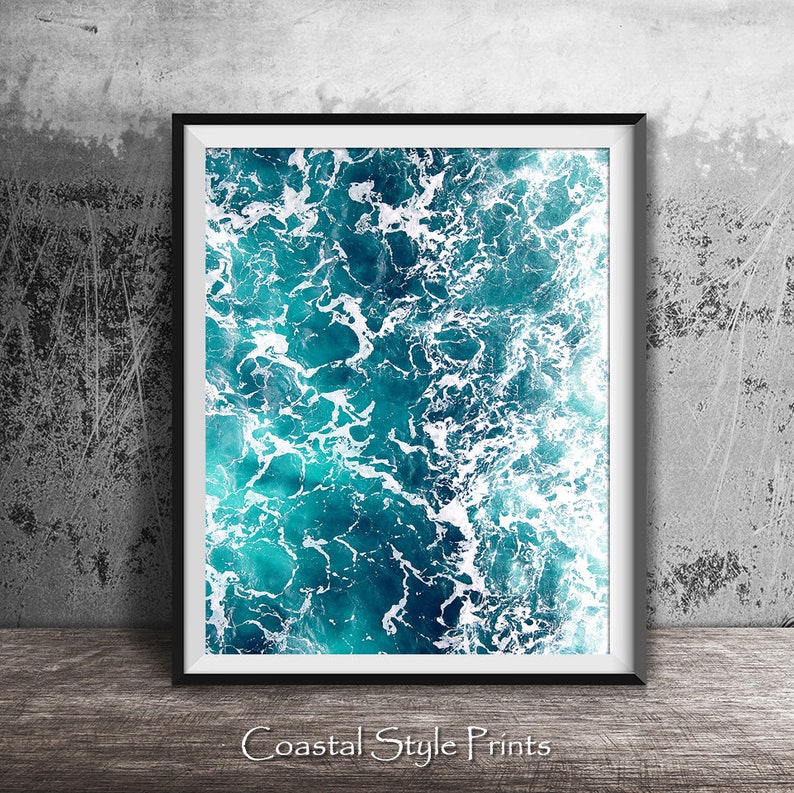 May include: A framed print of an abstract ocean scene with blue and white colors. The image shows a close-up of the ocean waves with white foam.