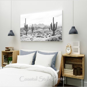 May include: Black and white photograph of a desert landscape with tall cacti in the foreground and mountains in the background.
