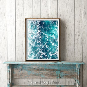May include: A framed photograph of a blue ocean with white foam waves. The photo is hanging on a light blue wooden wall.