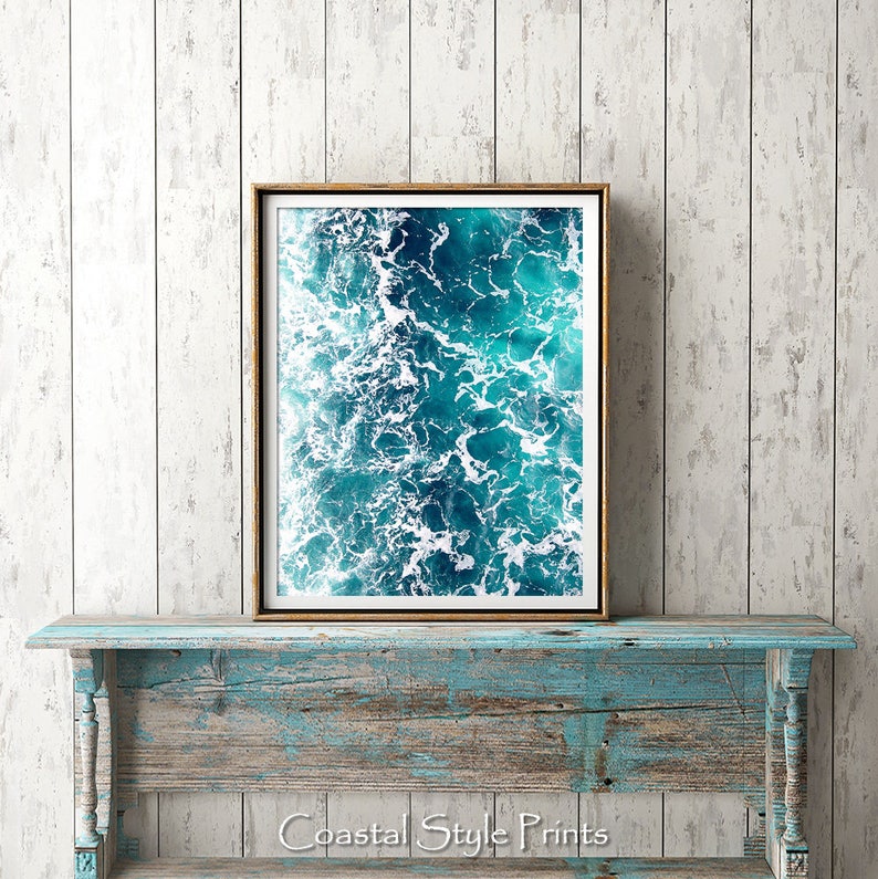 May include: A framed photograph of a blue ocean with white foam waves. The photo is hanging on a light blue wooden wall.