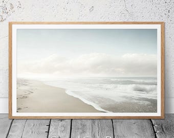 Könnte beinhalten: Ein gerahmtes Foto einer Strandszene mit weißem Sand, schaumigen Wellen und einem bewölkten Himmel. Das Foto ist in einem hellen Holzrahmen.