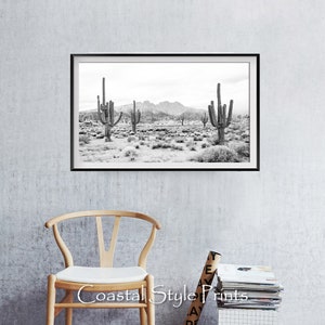 May include: Black and white photograph of a desert landscape with tall cacti in the foreground and mountains in the background.