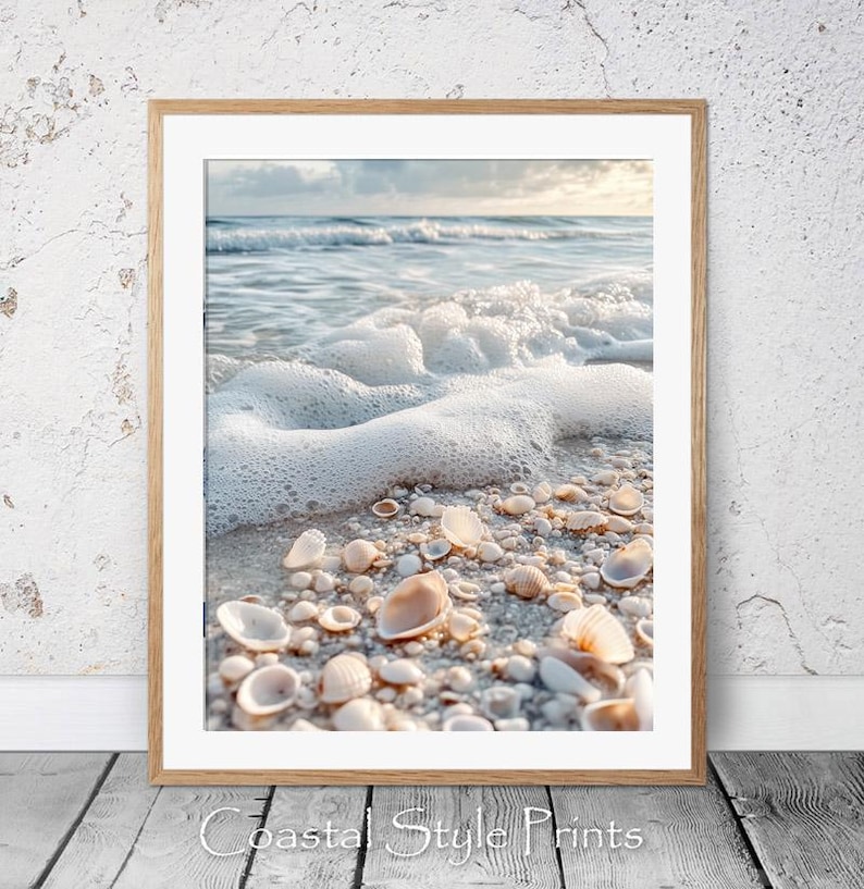 May include: A close-up of white seashells scattered on a sandy beach with foamy ocean waves in the background. The shells are various sizes and shapes, with some partially submerged in the sand.