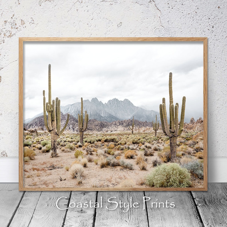 May include: A desert landscape with tall cacti in the foreground and a mountain range in the background. The sky is cloudy and the ground is sandy.