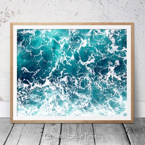 May include: An abstract aerial photograph of turquoise ocean water with white foam waves. The image is a close-up of the water and waves, creating a textured and dynamic pattern.
