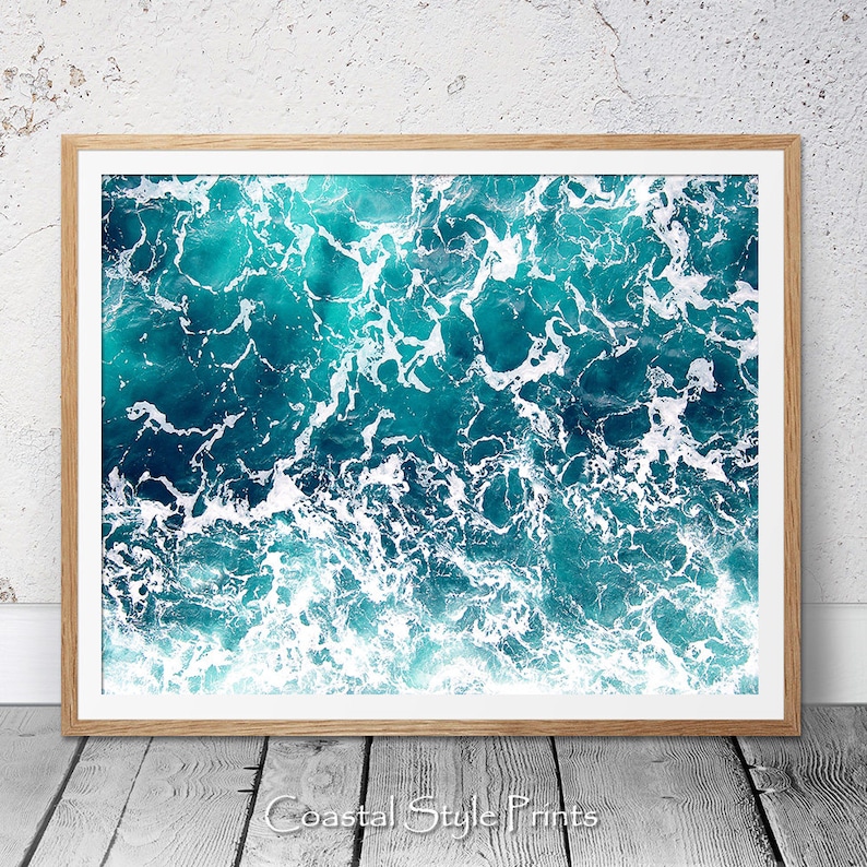 May include: An abstract aerial photograph of turquoise ocean water with white foam waves. The image is a close-up of the water and waves, creating a textured and dynamic pattern.
