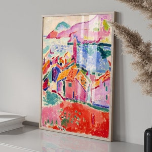 May include: A framed abstract painting of a coastal town with colorful buildings and a blue body of water in the background. The painting is done in a style reminiscent of Fauvism, with bold colors and brushstrokes.
