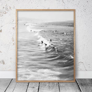 Könnte beinhalten: Schwarzweißfoto von Surfern, die auf Wellen am Strand reiten. Das Foto ist in einem hellen Holzrahmen gerahmt.