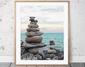May include: A framed photograph of a rock stack on a beach with a turquoise ocean in the background. The sky is a light blue with white clouds.