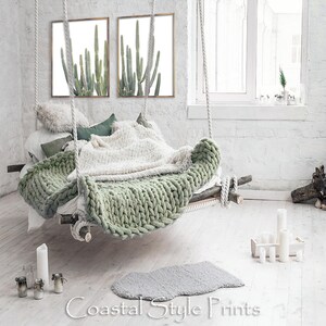 May include: Two framed prints of green cactus plants against a white background. The prints are hanging on a white brick wall above a hanging bed with a green and white knitted blanket.