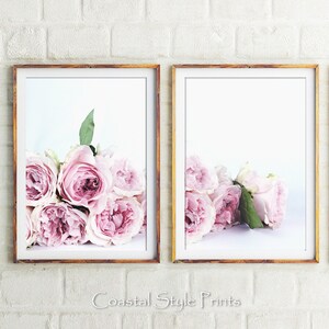 May include: Two framed prints of pink roses, each with a different arrangement of the flowers. The prints are in simple white frames with a light wood finish.