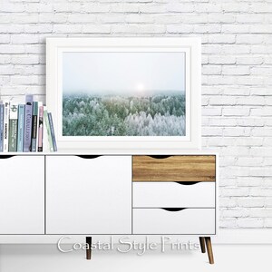 May include: A white dresser with three drawers, two white and one wood, sits in front of a white brick wall. A white frame with a photograph of a snowy forest hangs above the dresser. The dresser has a wooden base and the text "Coastal Style Prints" is printed below the dresser.