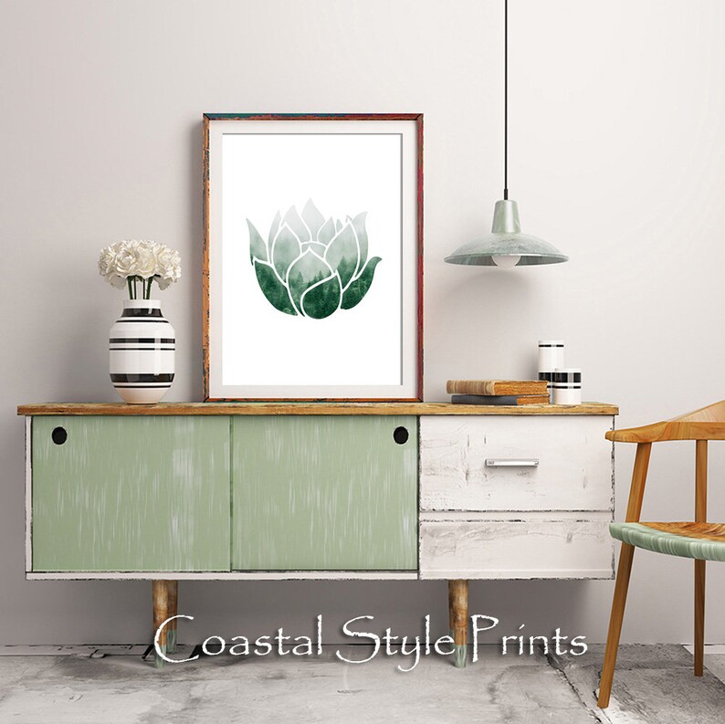May include: A framed print of a watercolor illustration of a green lotus flower. The print is hanging on a white wall above a light green and white dresser. The dresser has two drawers and a shelf. There is a chair to the right of the dresser.