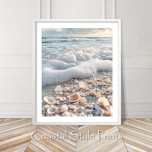 May include: A close-up of a sandy beach with white foamy waves crashing on the shore.  Seashells of various sizes and shapes are scattered on the sand.