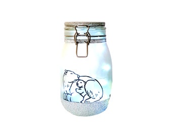 May include: A white glass jar with a silver lid and a silver glitter design. The jar has a polar bear and cub drawn on it. The jar is lit from inside with white lights.
