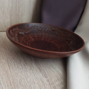 May include: A brown ceramic bowl with a decorative design of leaves and flowers around the rim.