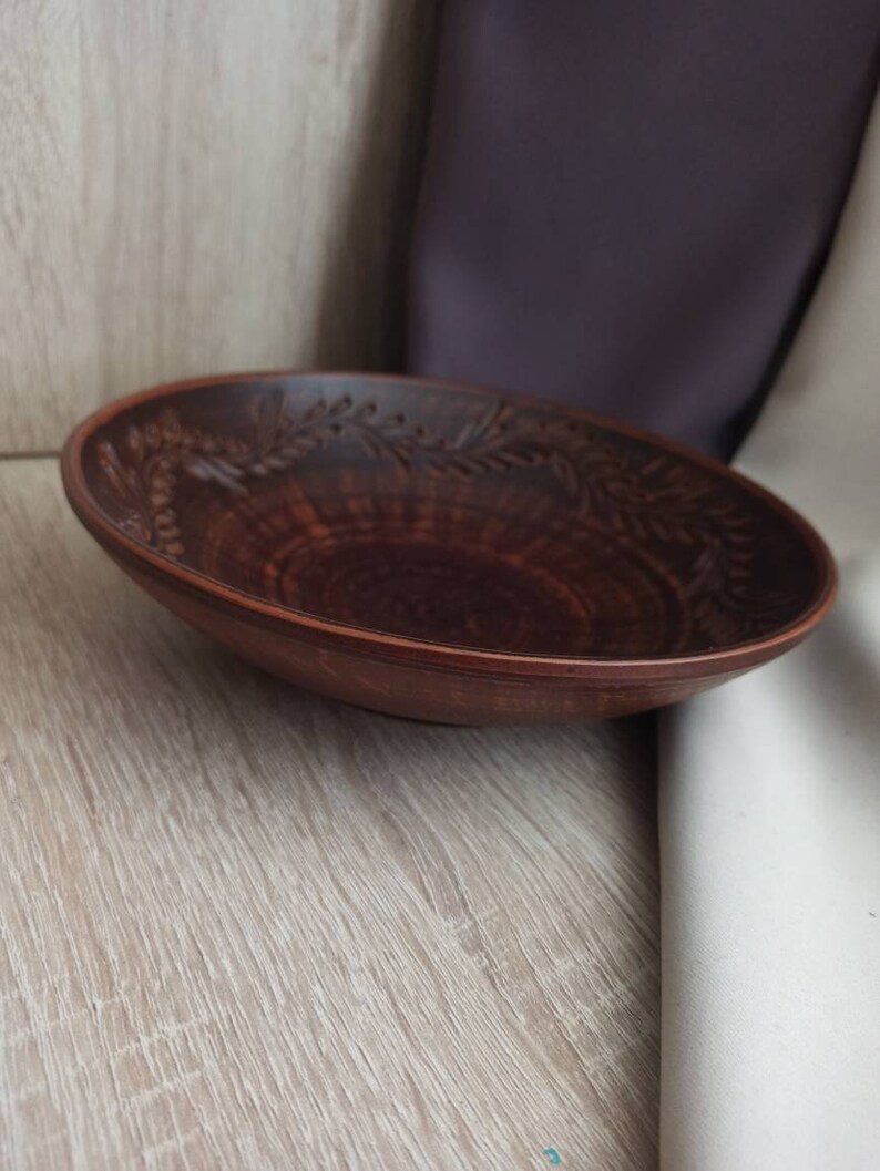 May include: A brown ceramic bowl with a decorative design of leaves and flowers around the rim.