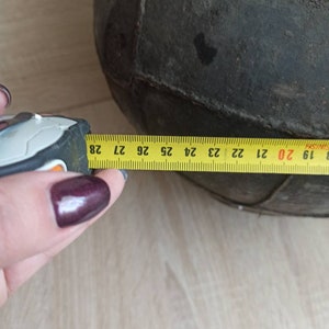 May include: A close-up of a black leather ball with a yellow measuring tape showing a circumference of 27 inches. The ball is made of stitched panels.