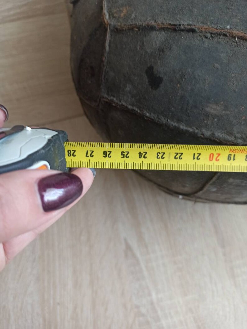 May include: A close-up of a black leather ball with a yellow measuring tape showing a circumference of 27 inches. The ball is made of stitched panels.