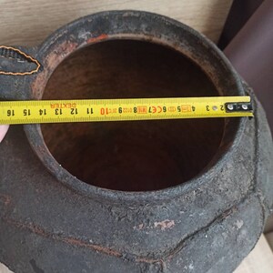 May include: A large, black, ceramic pot with a textured, geometric pattern. The pot has a wide opening and a rounded bottom. The pot is approximately 16 inches in diameter.