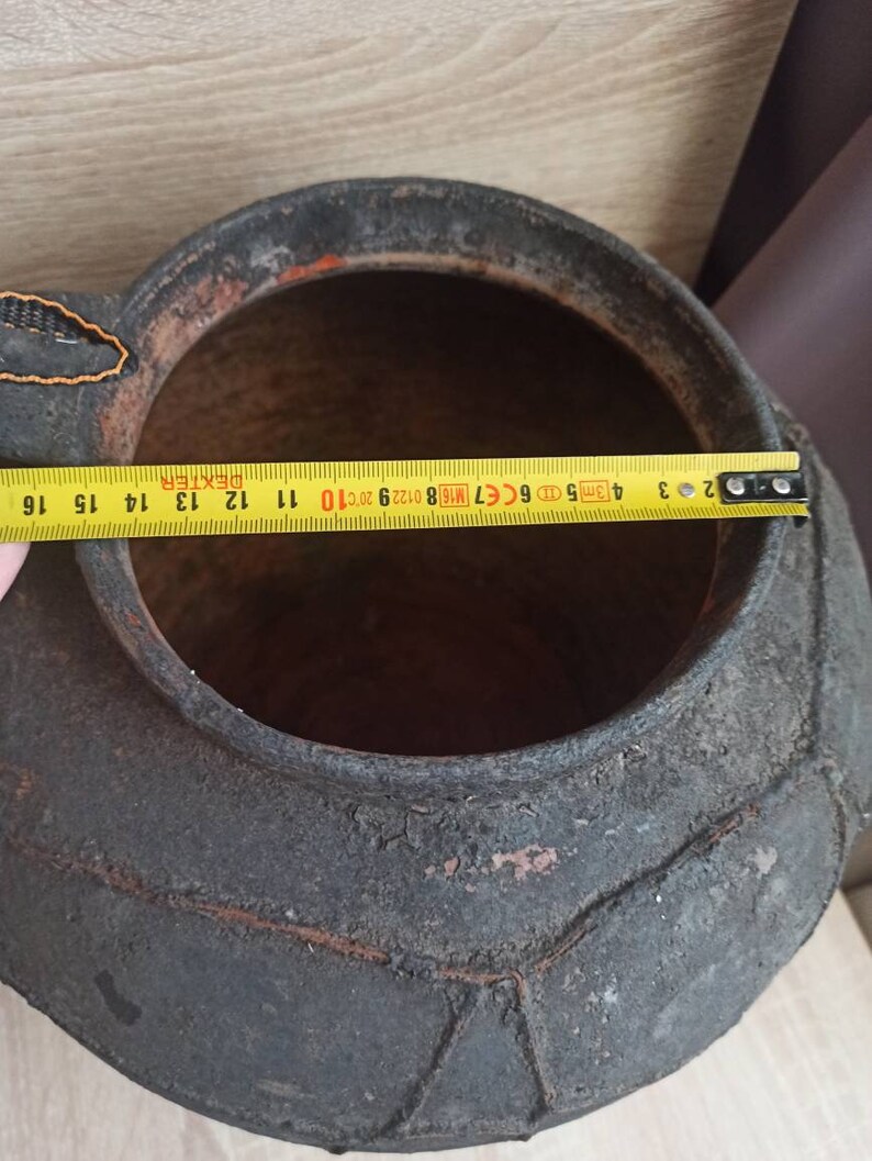 May include: A large, black, ceramic pot with a textured, geometric pattern. The pot has a wide opening and a rounded bottom. The pot is approximately 16 inches in diameter.