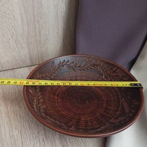 May include: A large, brown, ceramic bowl with a decorative design of leaves around the rim. The bowl is 23 inches in diameter.