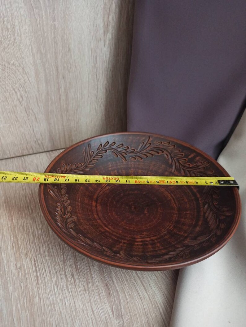 May include: A large, brown, ceramic bowl with a decorative design of leaves around the rim. The bowl is 23 inches in diameter.