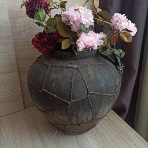 May include: A dark brown, leather-bound vase with a woven pattern, filled with pink and burgundy flowers.