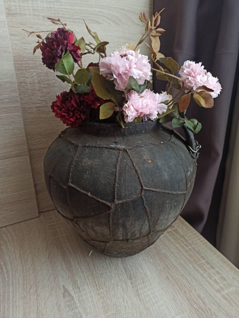 May include: A dark brown, leather-bound vase with a woven pattern, filled with pink and burgundy flowers.