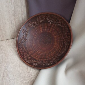 May include: A brown ceramic plate with a decorative design of leaves around the rim.