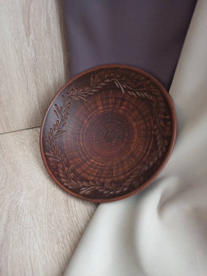 May include: A brown ceramic plate with a decorative design of leaves around the rim.