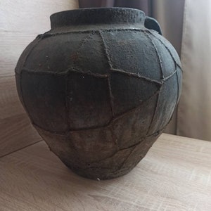 May include: A large, dark gray, ceramic pot with a woven pattern. The pot has a wide mouth and a rounded body.