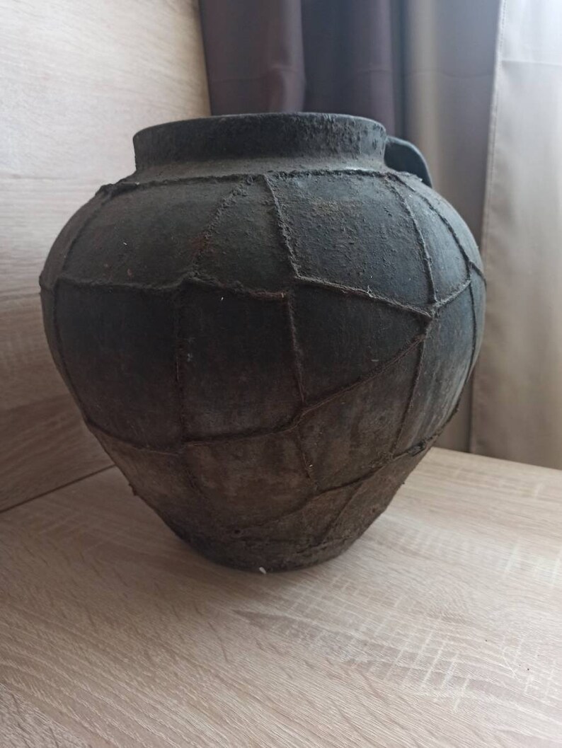 May include: A large, dark gray, ceramic pot with a woven pattern. The pot has a wide mouth and a rounded body.