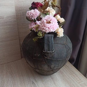 May include: A black, leather-wrapped vase with a metal handle, filled with pink and white silk flowers.