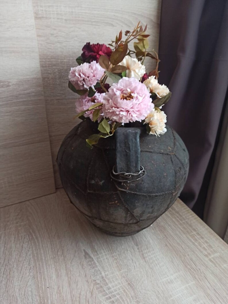 May include: A black, leather-wrapped vase with a metal handle, filled with pink and white silk flowers.