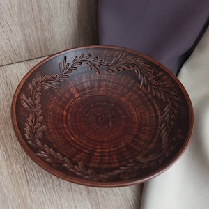 May include: A brown ceramic bowl with a decorative design of leaves around the rim.