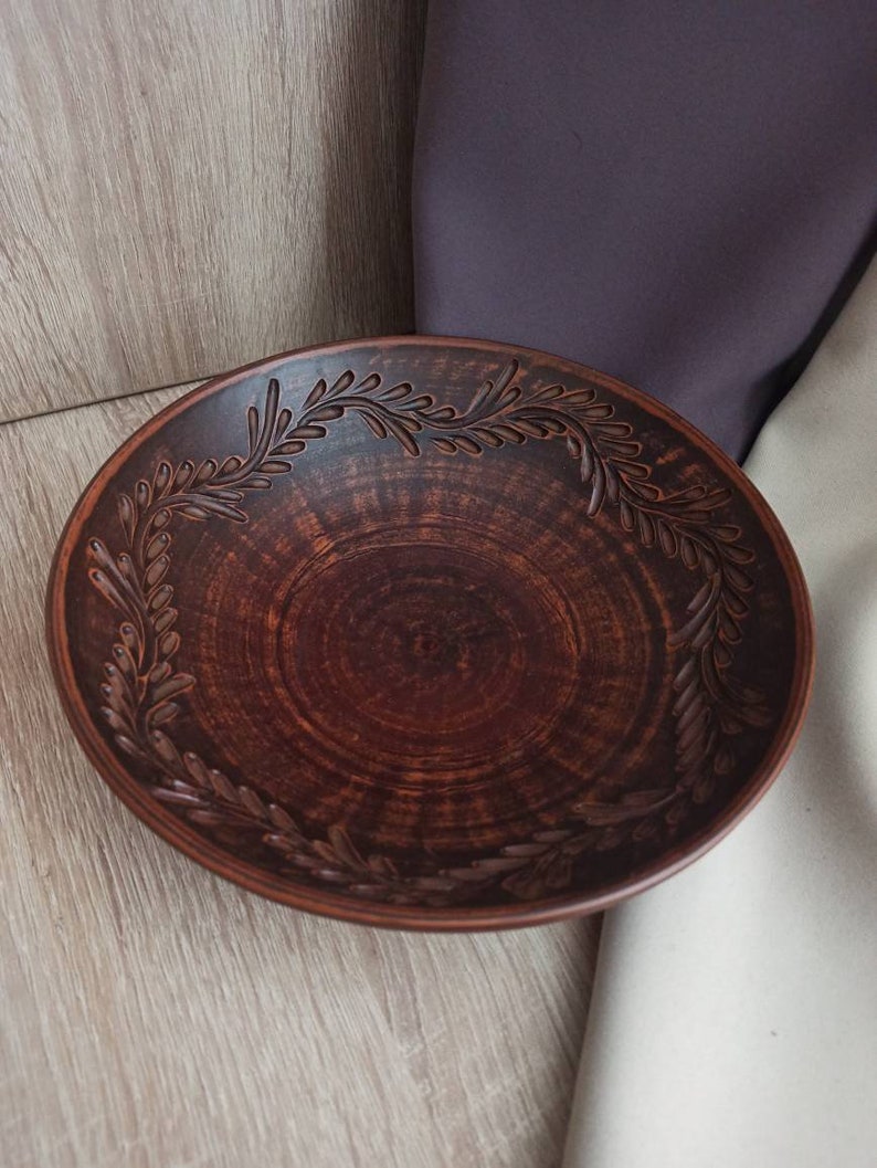 May include: A brown ceramic bowl with a decorative design of leaves around the rim.