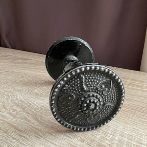 以下が含まれることがあります： 装飾的なデザインが施された黒い金属製のドアノブ。ノブは丸いベースと、隆起したデザインが施された丸いトップを持っています。