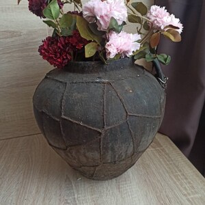May include: A dark brown, textured ceramic vase with a unique, geometric design. The vase is filled with pink and burgundy artificial flowers.