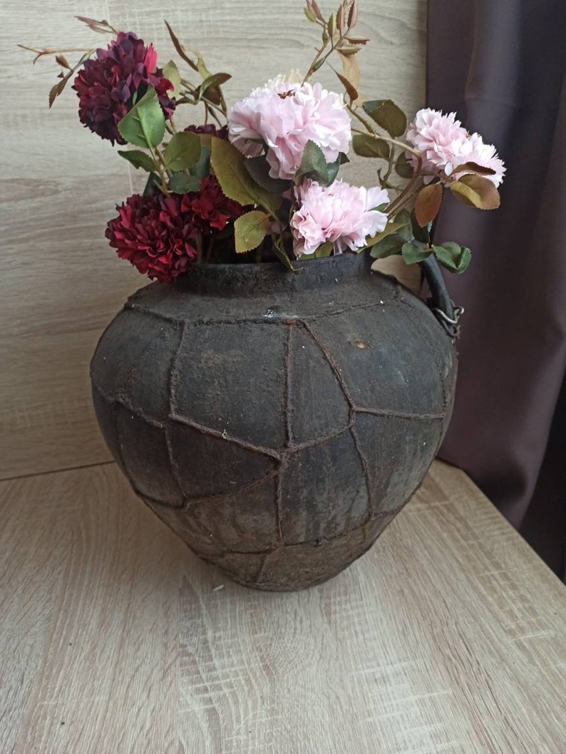 May include: A dark brown, textured ceramic vase with a unique, geometric design. The vase is filled with pink and burgundy artificial flowers.