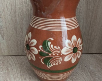 Pode incluir: Um vaso de cerâmica marrom com desenhos florais brancos e verdes. O vaso tem uma boca larga e um corpo arredondado.